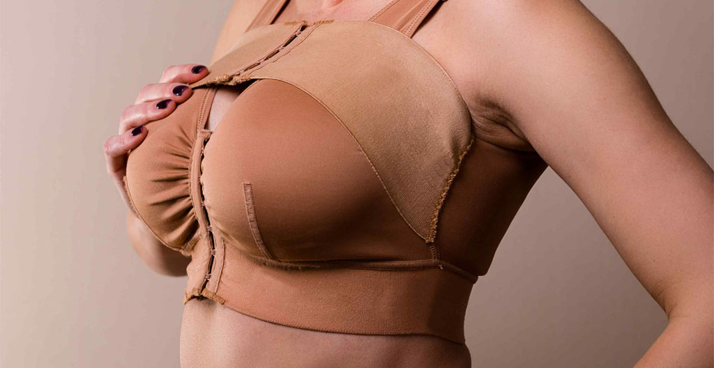 Une femme vue de dos dans une chambre lumineuse porte un soutien-gorge de contention, dans une atmosphère sereine de récupération